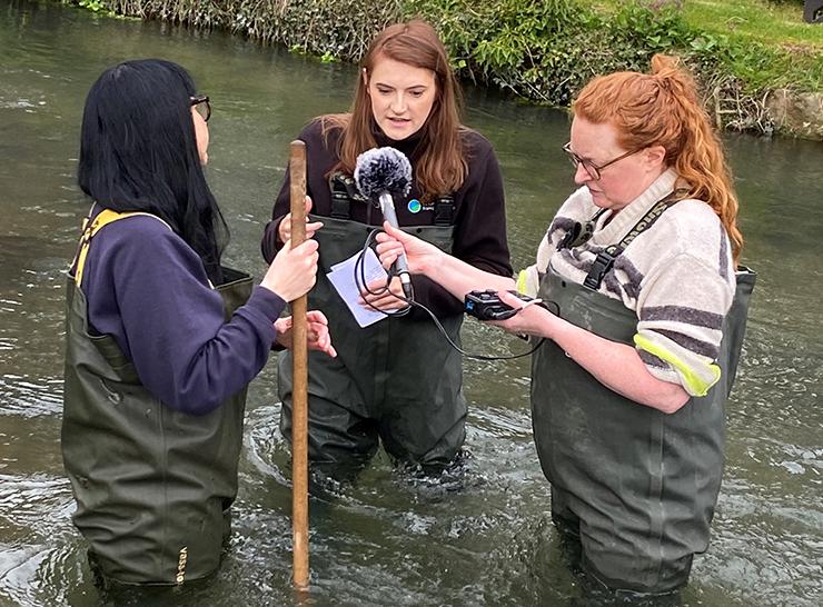 Three people standing in a river recording a podcast